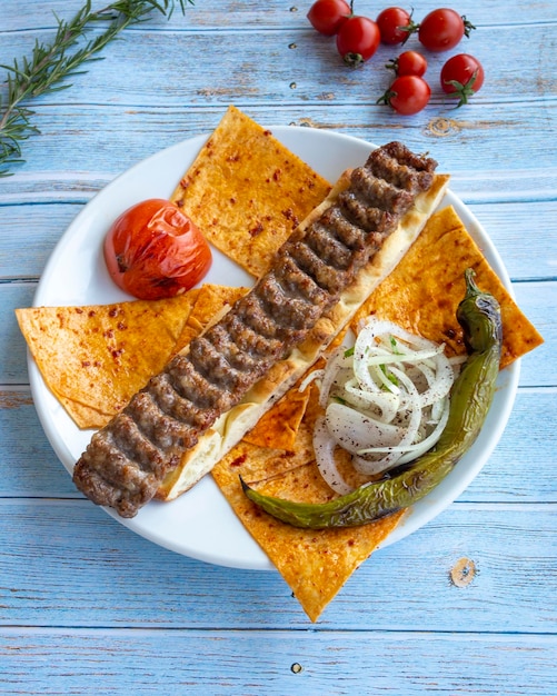 Adana kebab turkish kebab with roasted tomatoes onions and peppers on blue wooden background