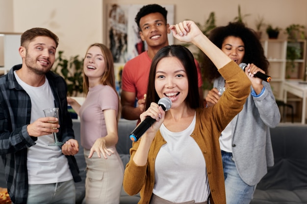 Photo add music to your party young pretty asian woman holding microphone and singing while having fun