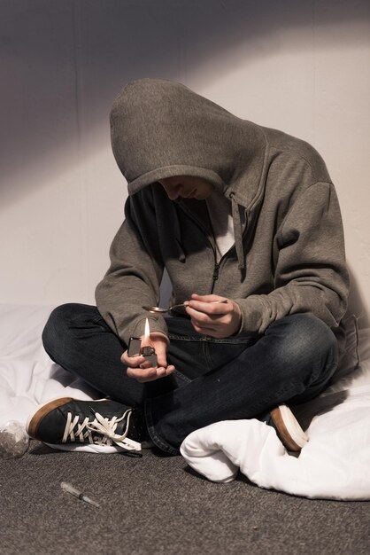 Photo addict man seating on bedding and heating spoon with heroin on lighter