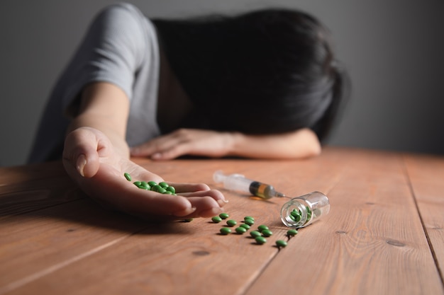 The addict reaches for the syringe and pills are spilled on the table