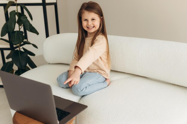 Addicted to modern technology joyful little cute girl sitting on the couch with a computer enjoying entertaining online games socializing on social networks watching funny video content