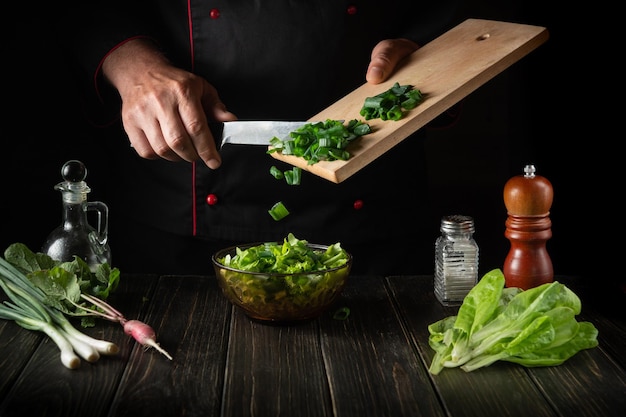 Adding chopped green onions to a fresh vegetable salad by the hands of a chef in the kitchen