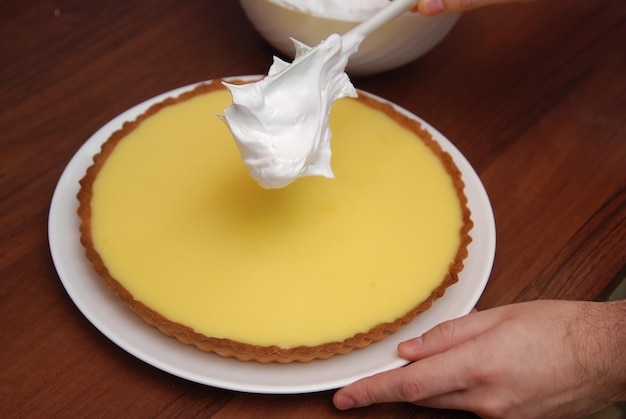 Aggiunta di crema di meringa su torta al limone su fondo di legno marrone. preparazione del dolce. torta sana fatta in casa.