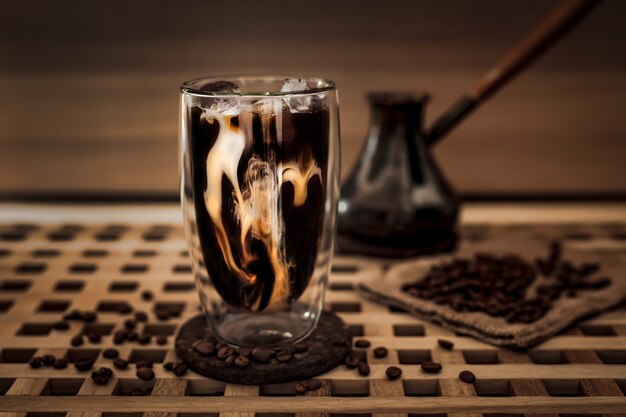 Adding milk to a big glass of iced coffee with coffee beans around