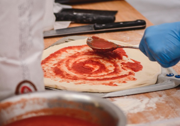 Photo adding tomato sauce with a spoon on pizza dough on a shovel on a wooden board close up