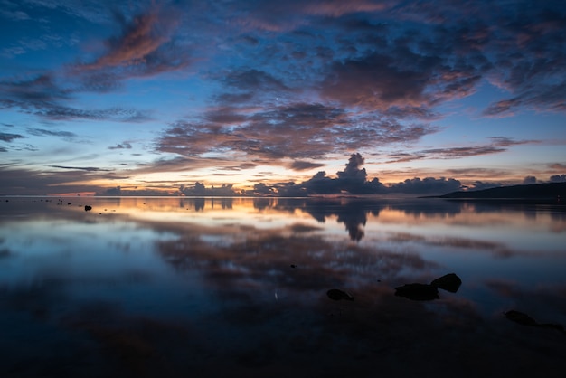 Adembenemende zonsopgang op het strand, kleurrijke wolken die als een spiegel in de gladde zee reflecteren.