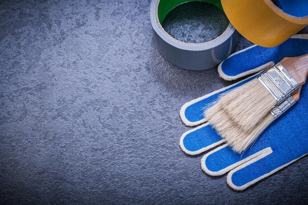 Adhesive tape paintbrushes working gloves on black background construction concept