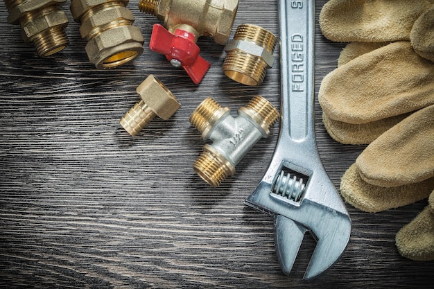 Adjustable wrench water valve pipe fittings safety gloves on wooden board.