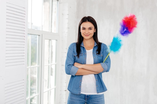 Admirable woman in denim standing with crossed arms and holding dust removing stick