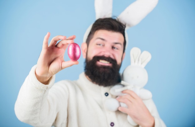 Восхищение яйцом Празднование весеннего праздника Бородатый мужчина с игрушкой-кроликом и пасхальным яйцом Пасхальный кролик доставляет крашеные яйца Хипстер с длинными кроличьими ушами держит зайца-несушку