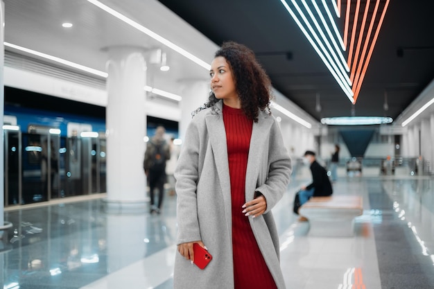 Admiring young woman with a smartphone standing on a subway platform