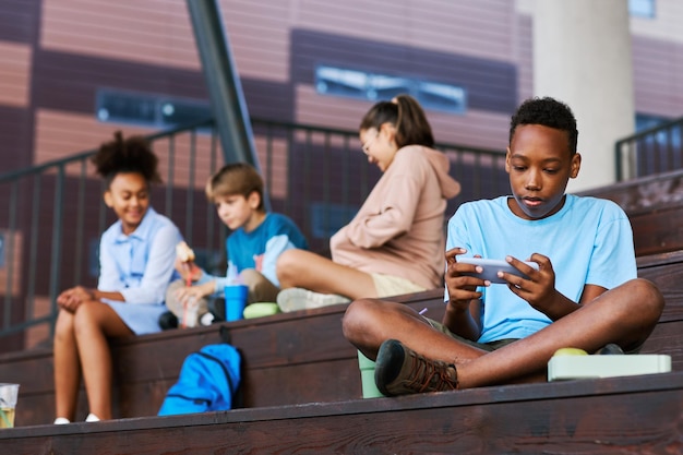 Adolescent African American schoolboy in casualwear using smartphone