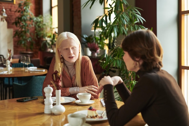 Adolescent albino girl sitting by table during communication with friend