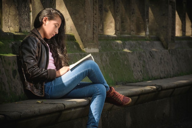 십대 소녀는 공원의 벤치에 앉아 책을 매우 주의 깊게 읽고 있습니다. 아름다운 날이고 독서를 즐깁니다.
