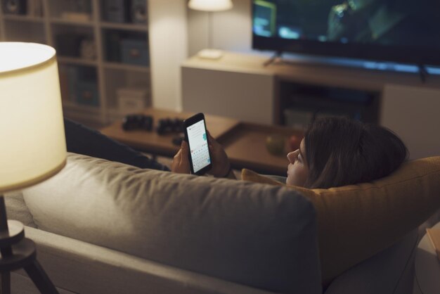 Ragazza adolescente sdraiata sul divano e connessa con il suo smartphone