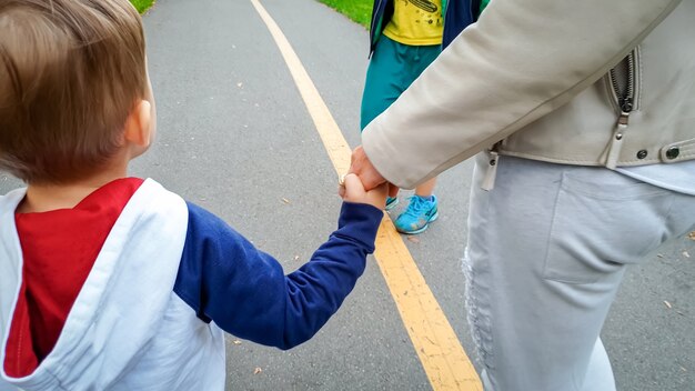 Adorable 3 years old toddler boy holding his mother by hand and walking on street