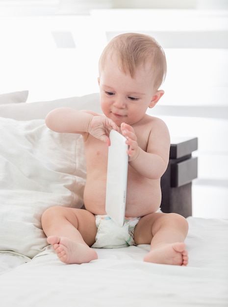 Adorabile bambino di 9 mesi che gioca con la tavoletta digitale sul letto