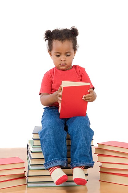 Photo adorable african baby reading sitting on a pile of books on a over white background