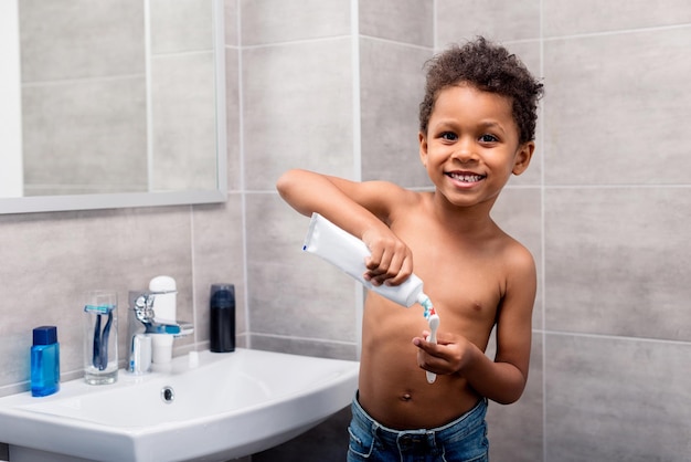 Очаровательный афроамериканский ребенок наносит зубную пасту на щетку