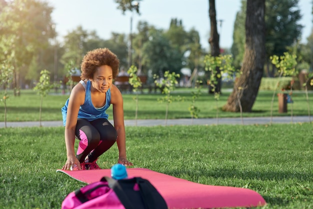 Adorable afro american girl rolling out yoga mat on grass