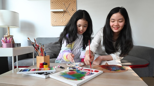 Adorable asian girls painting picture on canvas together at home