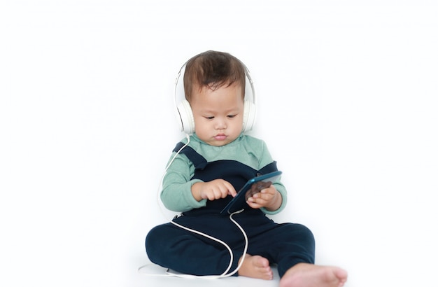 Adorable asian little baby boy enjoys listening music with headphones by smartphone