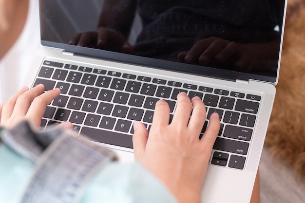 Adorable Asian smart girl in casual playing game or studying at home on laptop