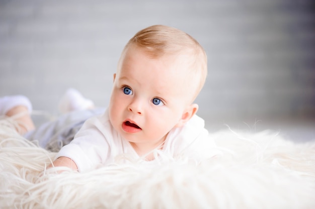 Adorable baby boy learning to crawl and playing in white sunny bedroom. Cute laughing child crawling on a fluffy mat.