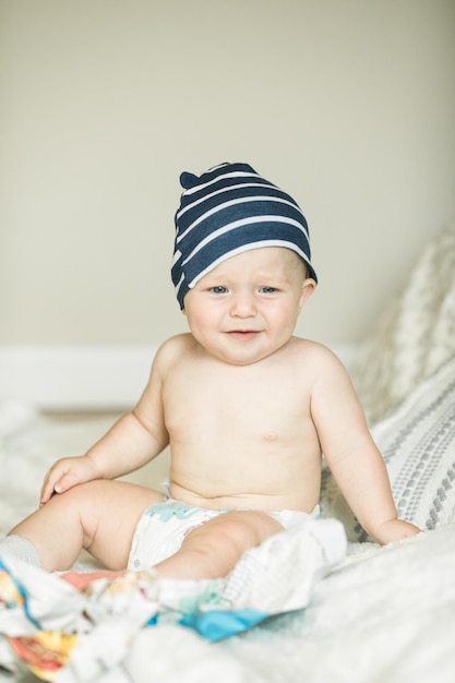 Adorable baby boy learning to crawl and playing with paper magazine in white sunny bedroom Cute laughing child seating on a rug Nursery clothing and toys for little kids