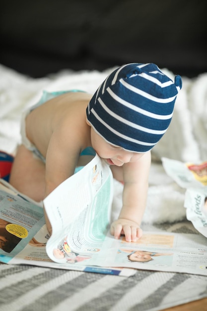 Adorable baby boy learning to crawl and playing with paper magazine in white sunny bedroom