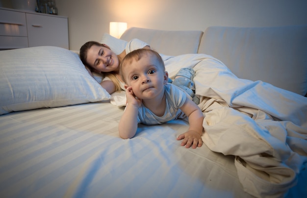 Adorable baby boy lying on bed next to his mother trying to sleep