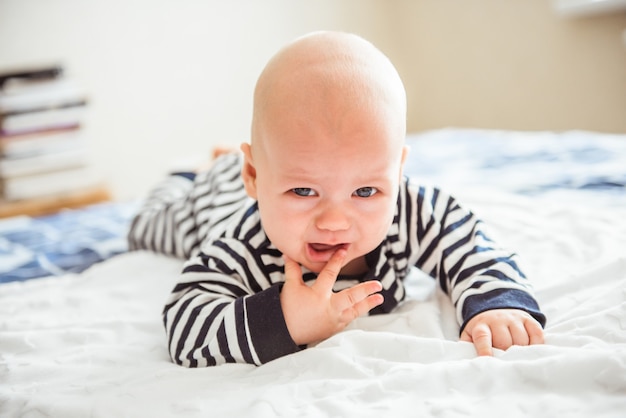 Adorable baby boy in white sunny bedroom. Newborn child relaxing in bed. Nursery for young children. Textile and bedding for kids. Family morning at home