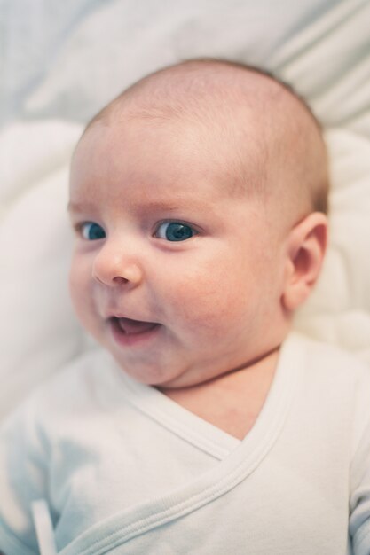 Adorable baby boy in white sunny bedroom. Newborn infant child relaxing in bed.