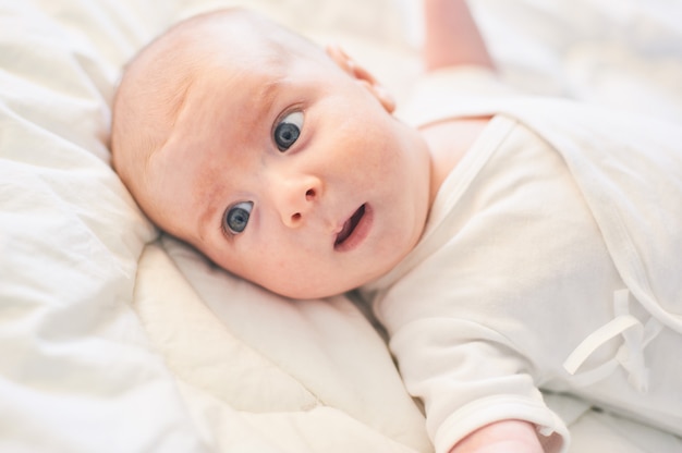 Adorable baby boy in white sunny bedroom. Newborn infant child relaxing in bed.