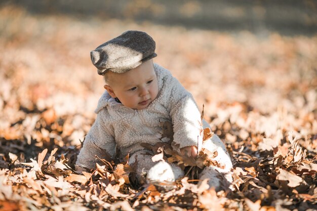 Foto adorabile bambino che striscia tra le foglie cadute alla luce del sole mattutino