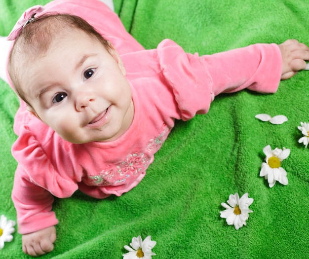 Adorable baby girl lying down on meadow and smile