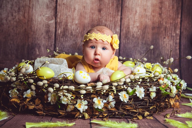 Adorable baby lying in giant nest decorated with easter eggs and feather easter tradition