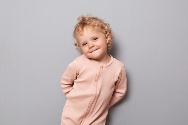 Adorable baby portrait Innocence and childhood joy Sweet cheerful toddler Cute funny baby girl with blonde wavy hair wearing rose shirt isolated over gray background smiling happily