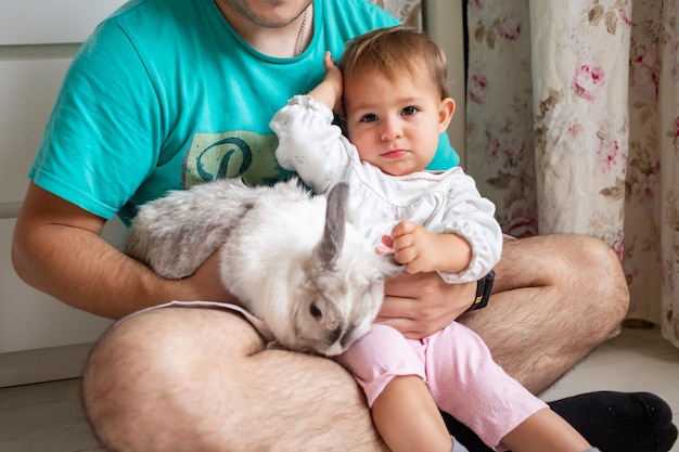 Adorable baby sits in dads arms and strokes a decorative rabbit\
domestic animals in a family with