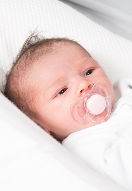 Adorable baby wearing a white clothe with a soother