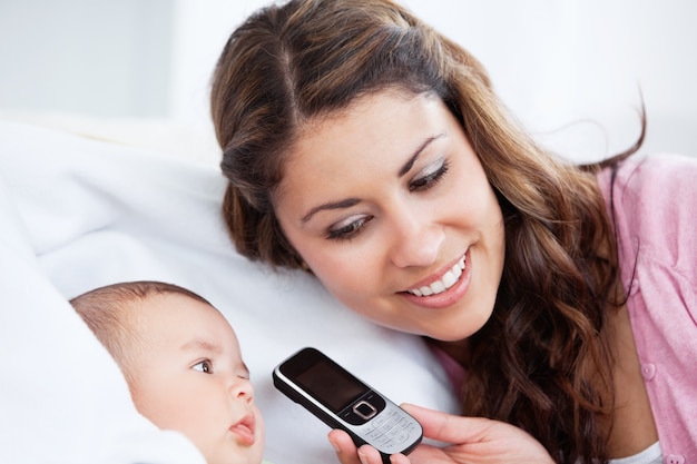 Adorabile bambino con sua madre sul divano cercando di parlare al telefono