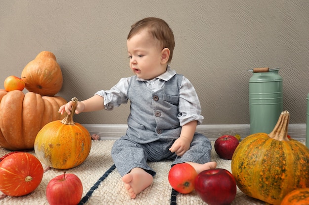 Adorable baby with ripe pumpkins and apples indoors