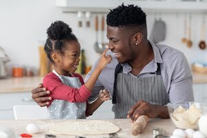 Photo adorable black girl making her father nose dirty with flour