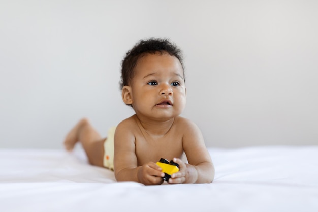 写真 ベッドに横たわっている間、おもちゃの車で遊ぶ愛らしい黒人幼児男の子