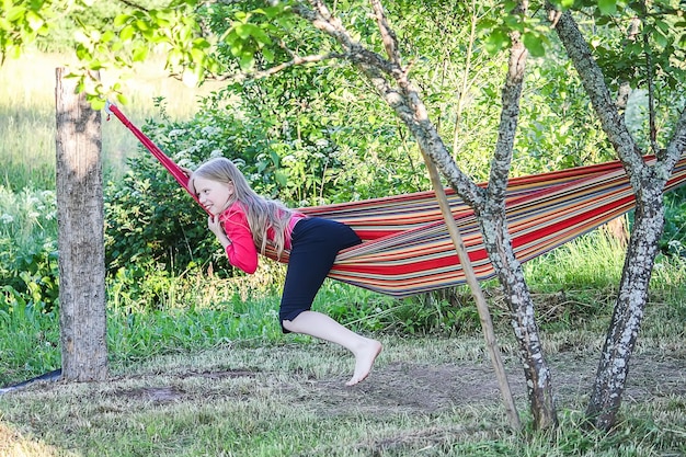 Photo adorable blonde girl in a striped hammack in summer park