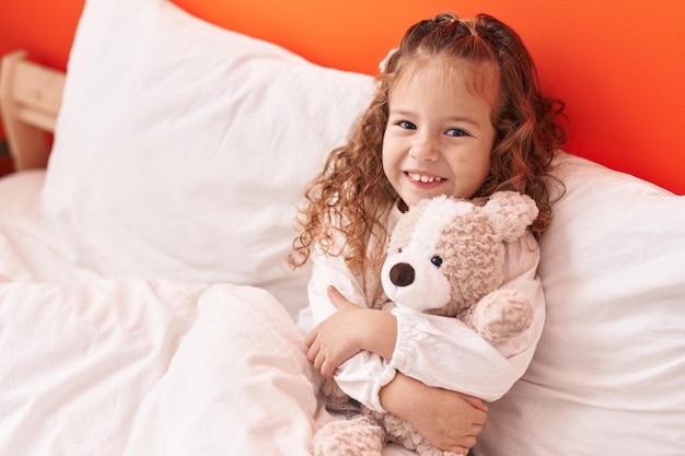 Adorable blonde toddler hugging teddy bear lying on bed at bedroom