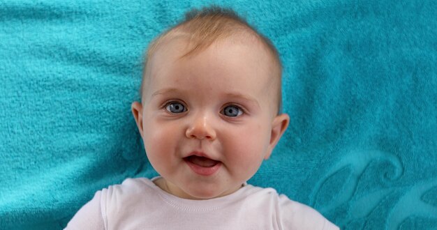 Adorable blue eyed baby with opened mouth lying on blue towel and looking at camera