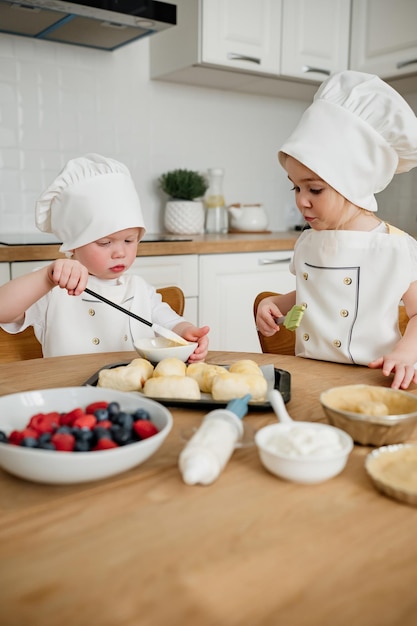 Adorable boy ad girl in chefs hats and aprons preparing sausage rolls