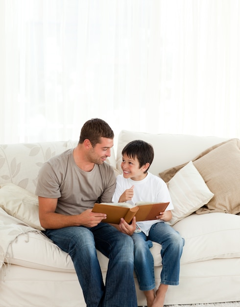 Adorable boy looking at a photo album with his father on the sofa 