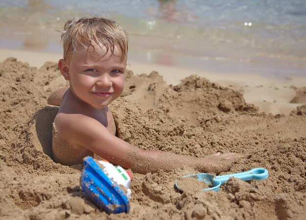 愛らしい少年は砂でビーチで遊ぶ